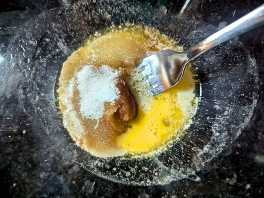 Image shows sugars, vanilla, brewed coffee, and egg added to melted butter in a mixing bowl.