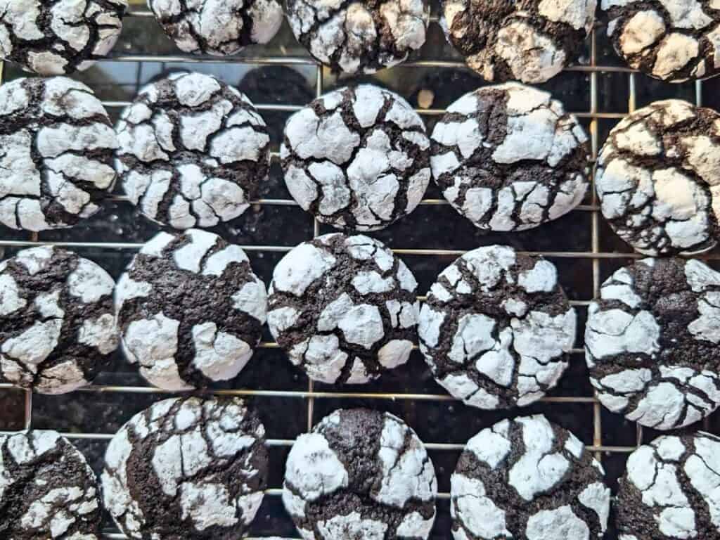 Rows of chocolate crinkle cookies with powdered sugar on top, cooling on a metal wire rack.