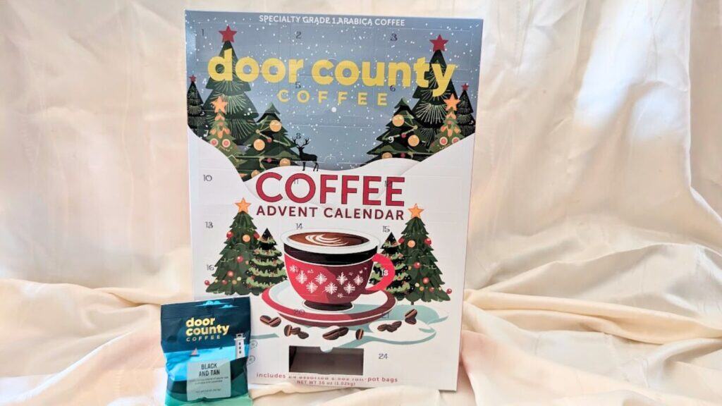 A festive Door County Coffee Advent Calendar box featuring trees and snow sits beside a packet labeled "Black Gold Roast," making it a perfect addition to your holiday collection of Advent calendars.