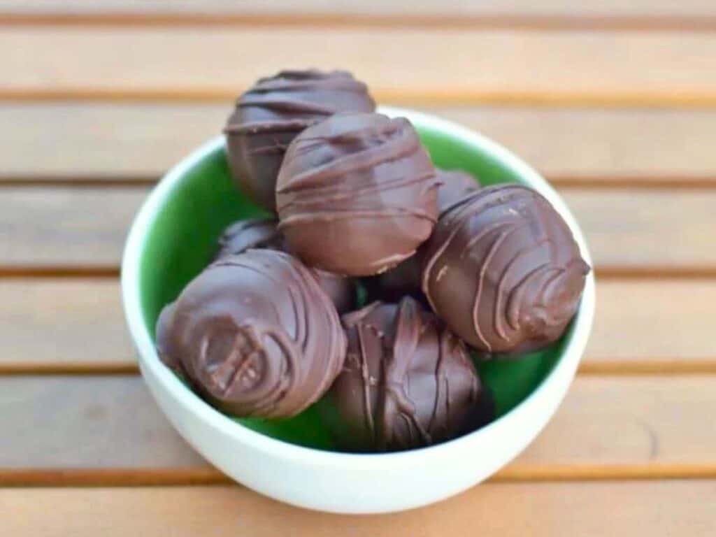 A white bowl filled with six chocolate-coated truffles sits on a wooden surface.