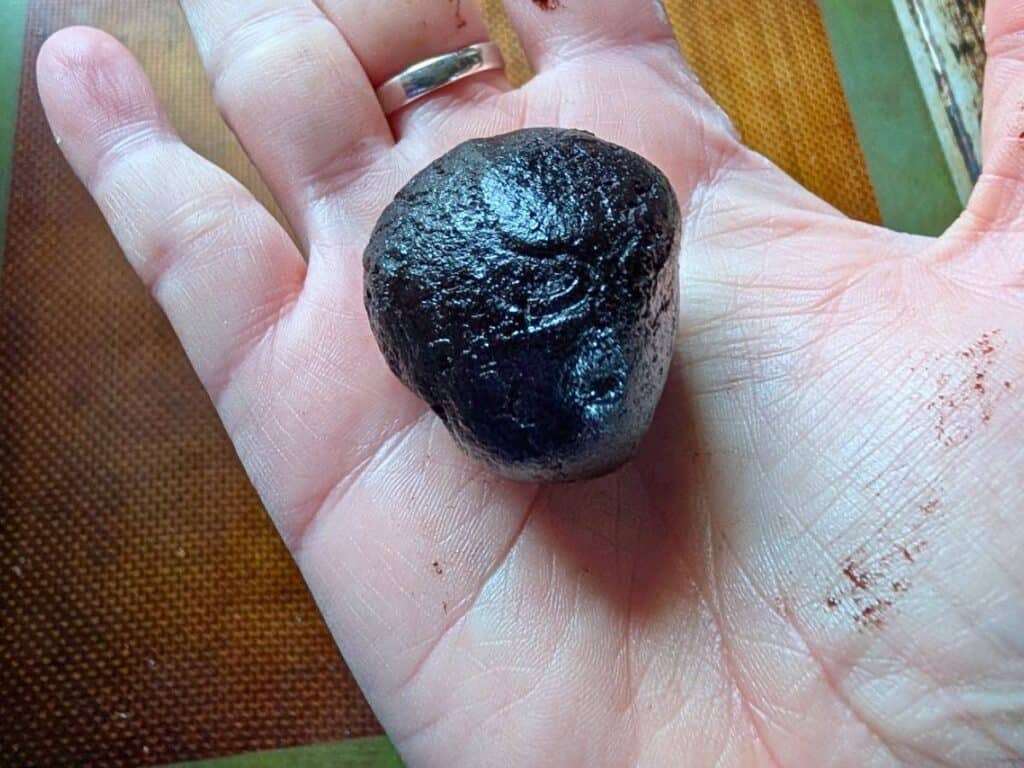A hand holding a round, dark brown ball of dough or batter, with some residue visible on the fingers.