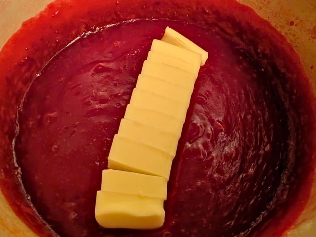 Several slices of butter placed on top of a thick red sauce in a pot.