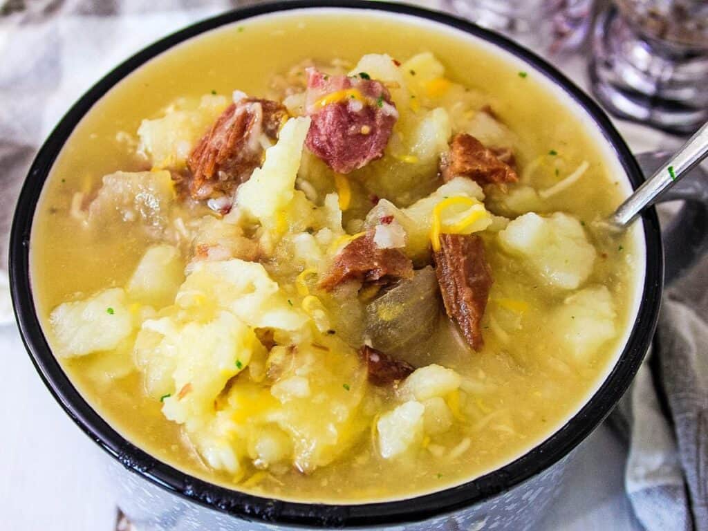 A bowl of hearty potato soup with chunks of potatoes and pieces of ham, served with a spoon.