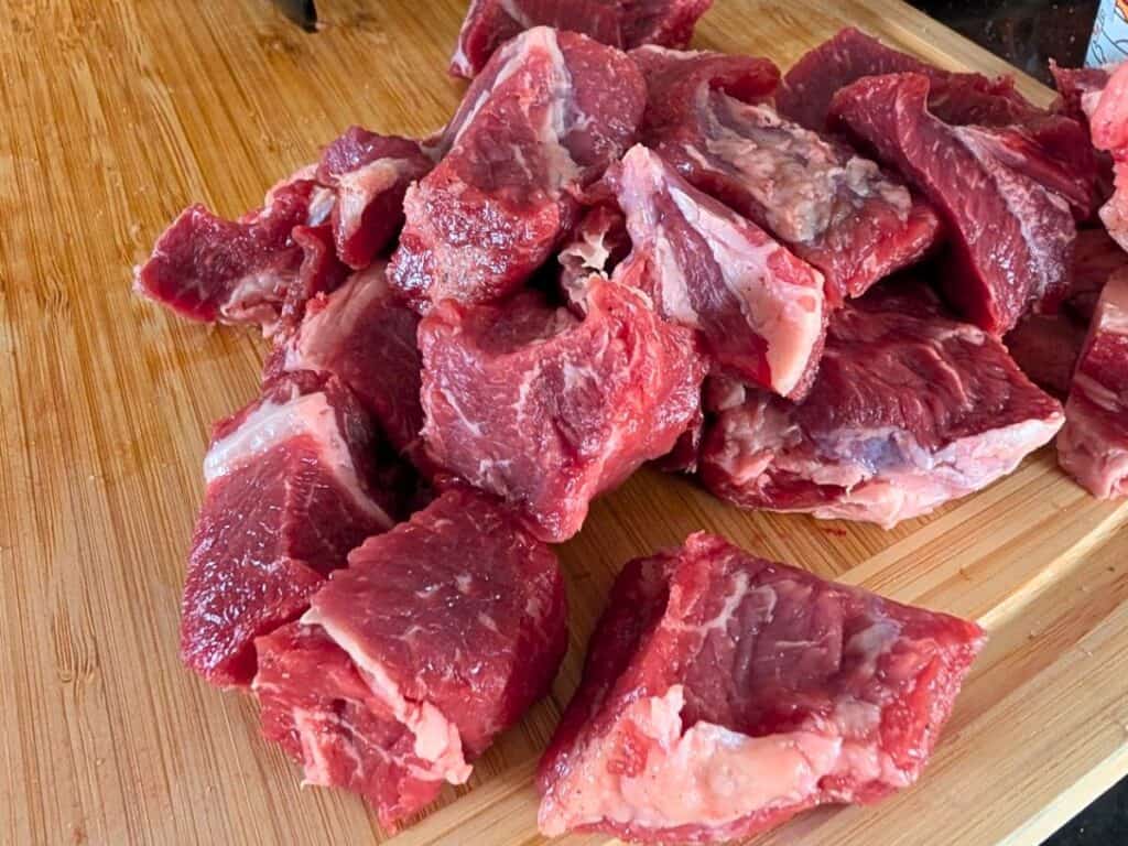 Chunks of raw beef placed on a wooden cutting board.