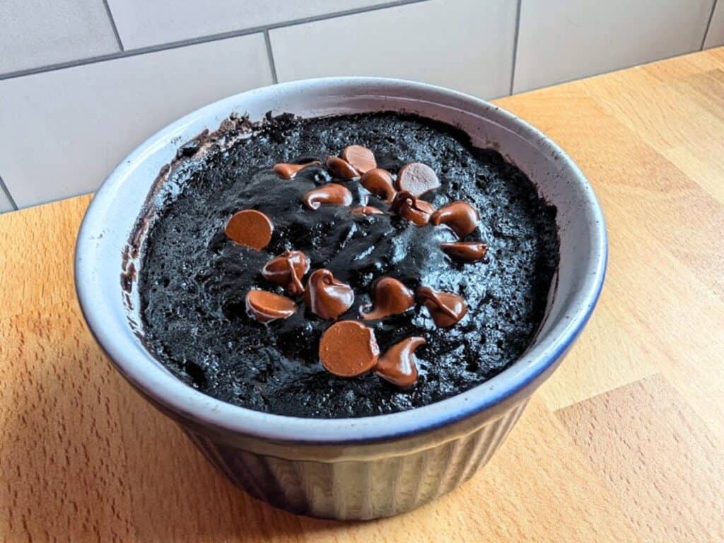 A chocolate mug cake with melted chocolate chips on top, served in a white ramekin on a wooden countertop.