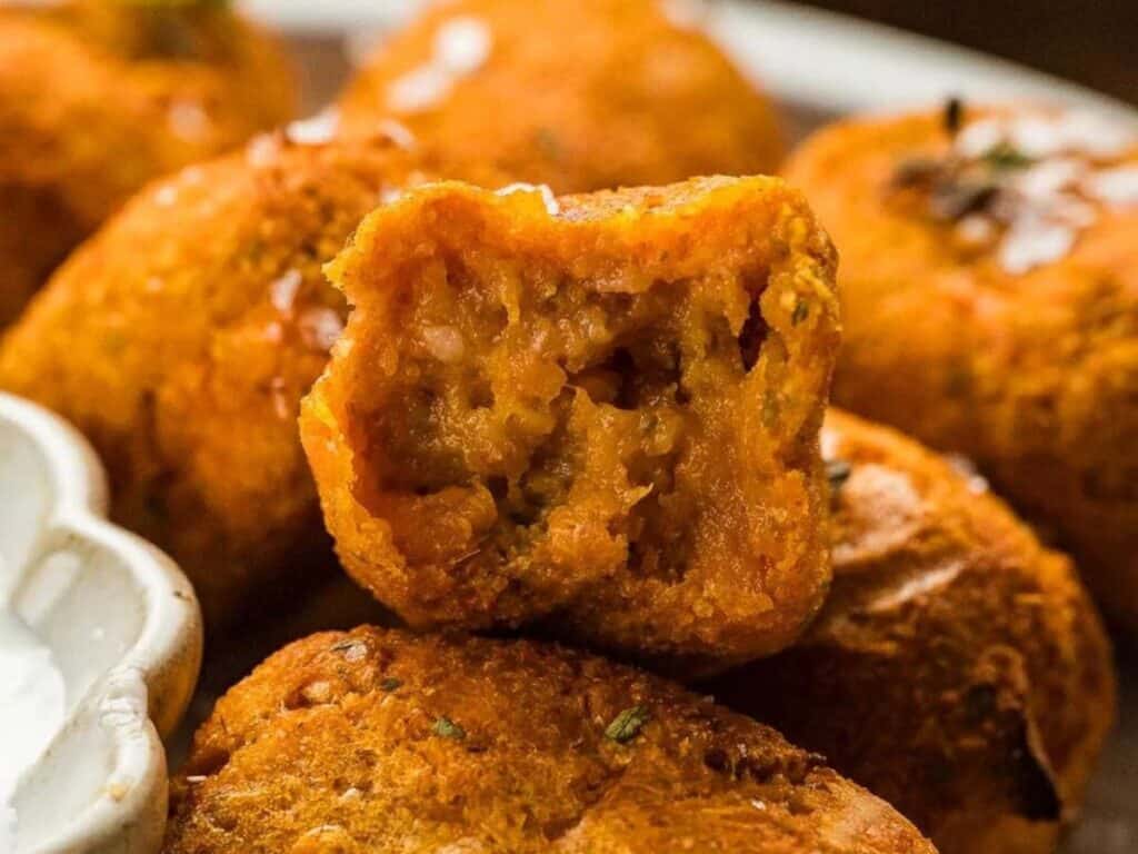 Close-up of a plate of fried snacks, with one piece broken open to show a spiced potato filling.