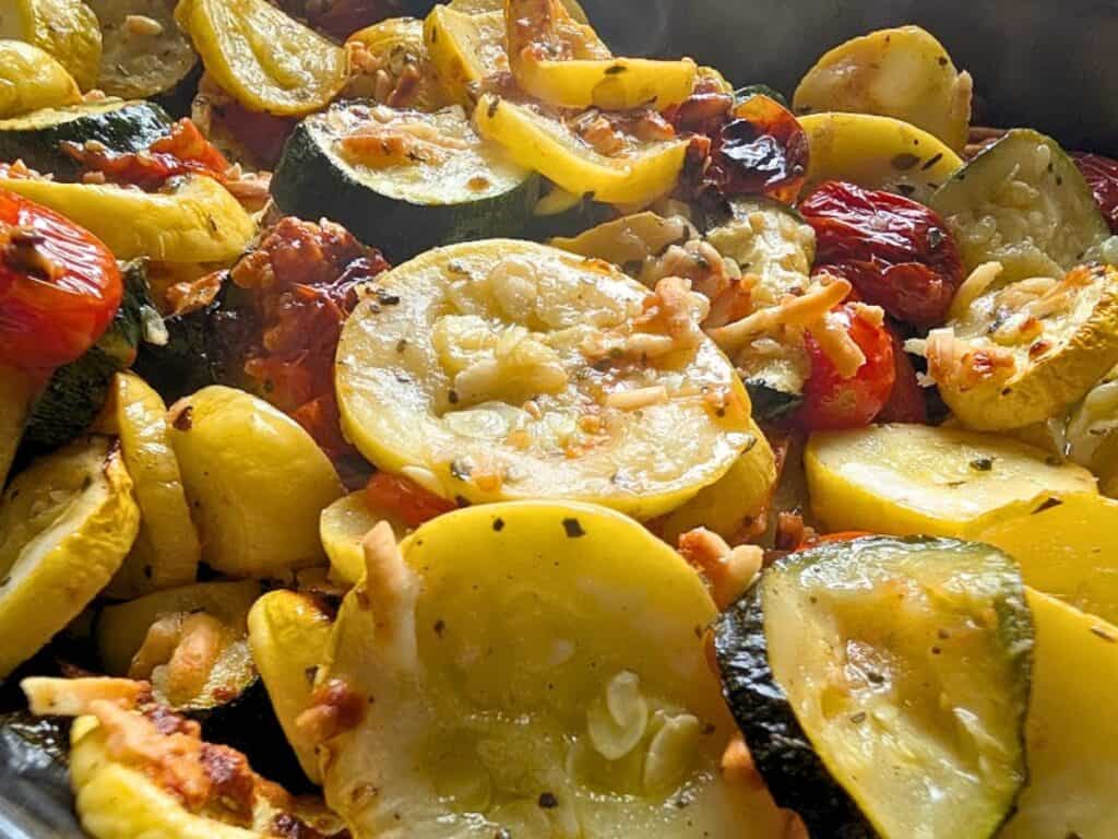 Close-up of sliced yellow squash, zucchini, and tomatoes baked with shredded cheese and herbs.