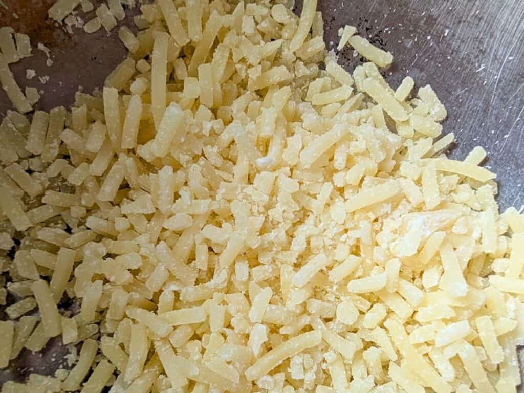 Shredded yellow cheese scattered on a metallic surface.