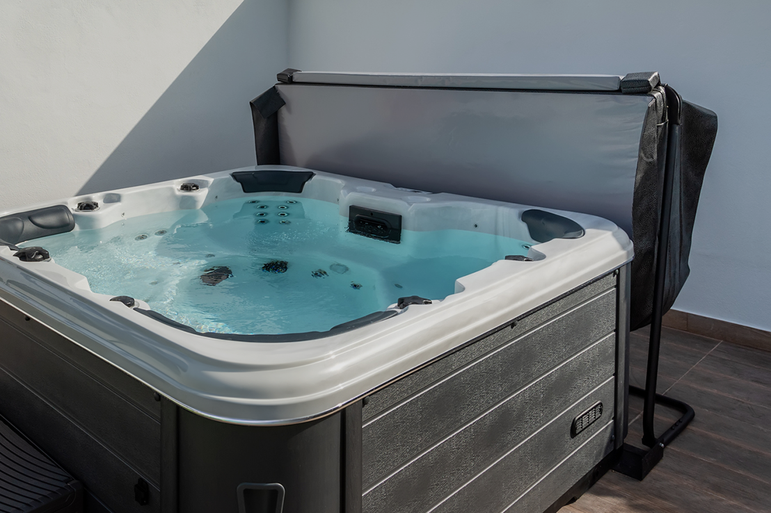 Black hot tub cover lift holding a spa cover open, revealing a modern outdoor hot tub with bubbling water.