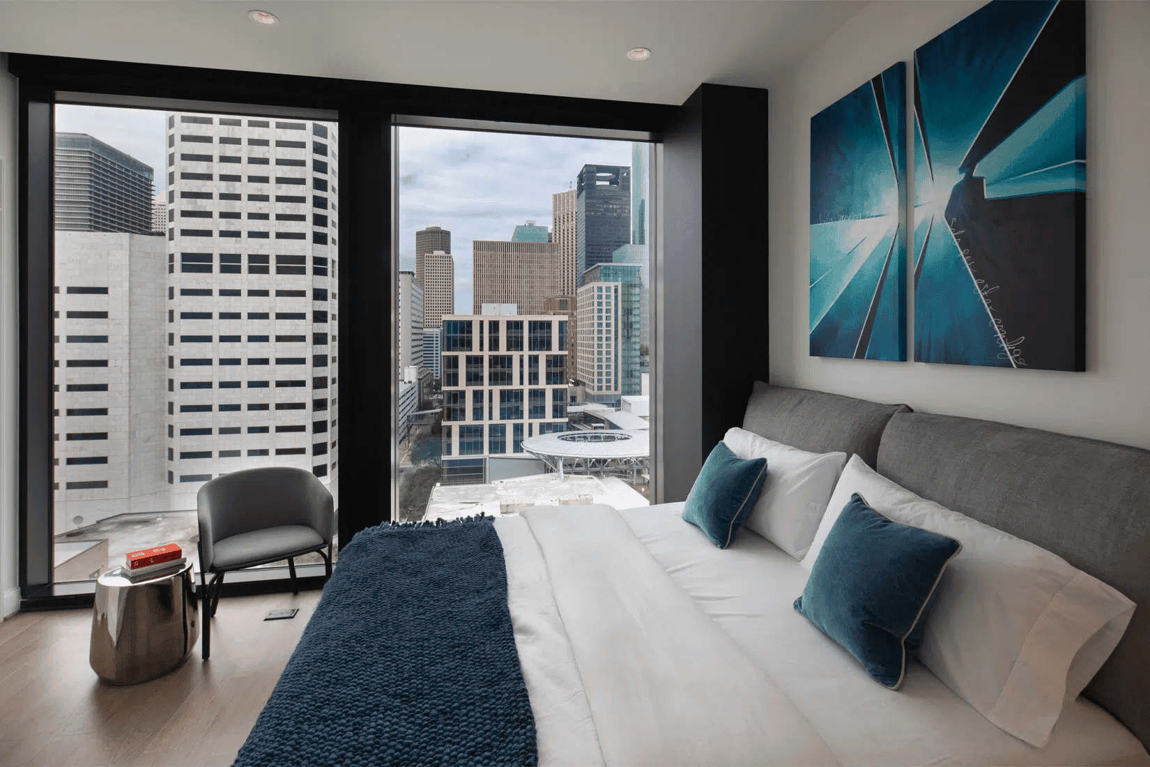 Luxurious modern bedroom with city skyline view in Houston EB5 investment properties. Floor-to-ceiling windows showcase downtown Houston's skyscrapers, offering a stylish and inviting living space.