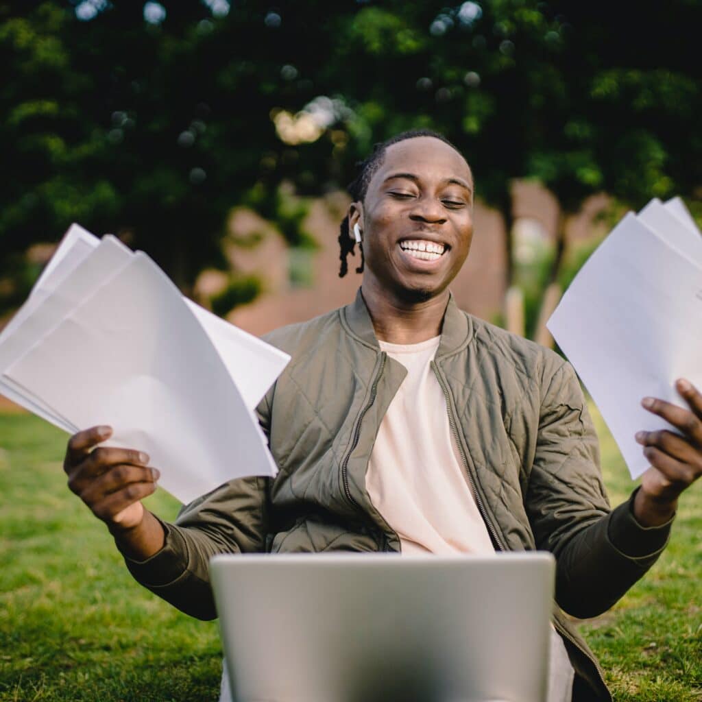 Multiethnic man enjoying paperwork outdoors, symbolizing success in Houston EB5 investment programs and visa process, with a laptop and documents in a park setting.