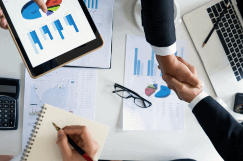 Strategic business partnership handshake at office desk with financial reports and devices, emphasizing Houston EB5 investment programs.