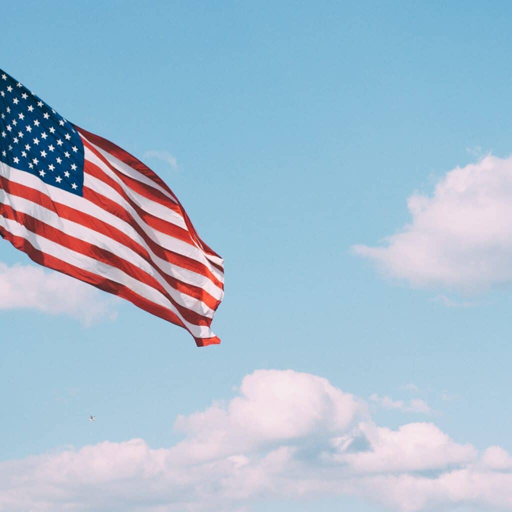 Bright American flag waving against a blue sky with white clouds, symbolizing U.S. patriotism, investment opportunities, and immigration via Houston EB5 programs.
