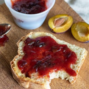 Plum and ginger jam on toast with a cut fresh plum next to it.
