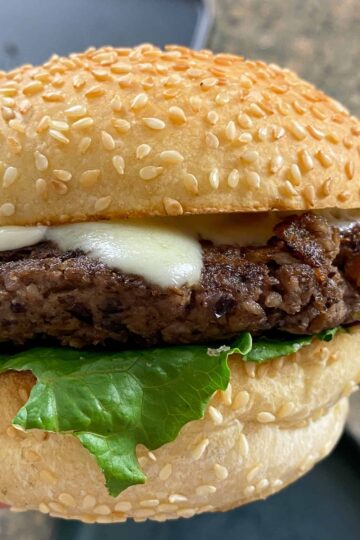 close-up shot of a mushroom walnut veggie burger with lettuce and cheese on a sesame seed bun.