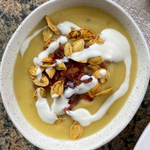 Rutabaga soup with crispy bacon, sour cream, and pumpkin seeds in a bowl.