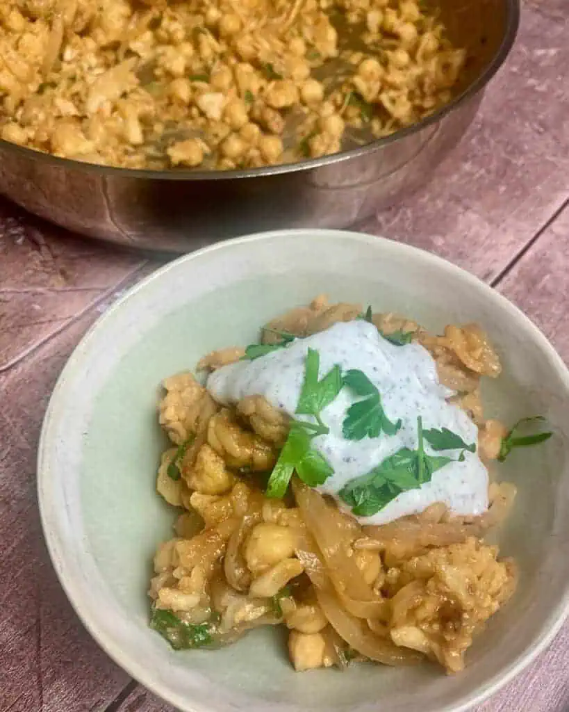 A bowl of baked orzo with yogurt sauce on top.