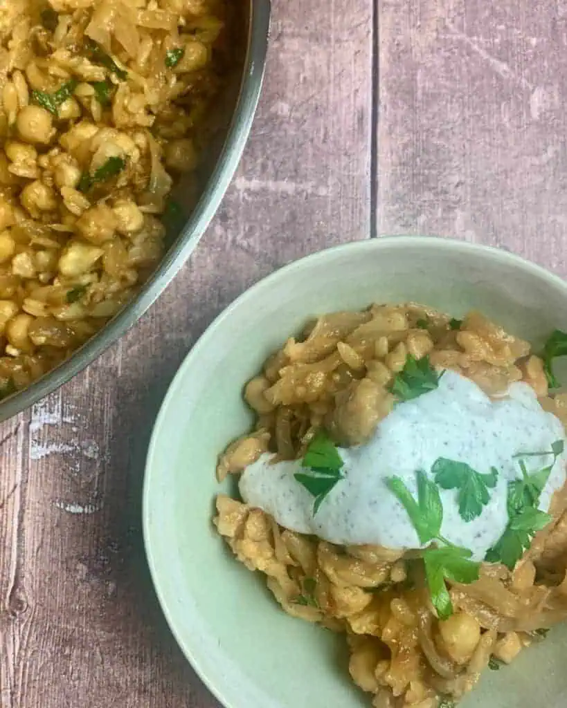 A bowl of baked orzo with yogurt sauce on top.