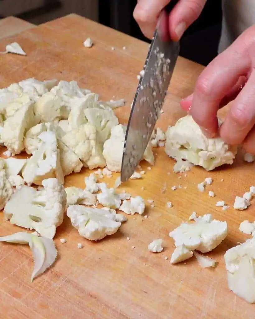 A woman chopping cauliflower on a wooden cutting board.