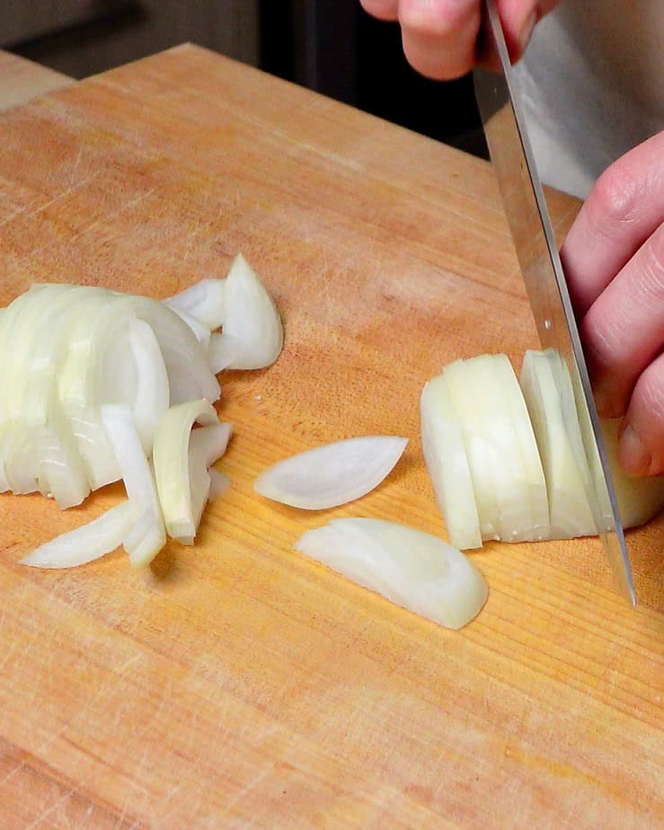 A woman slicing an onion on a woodin cutting board.