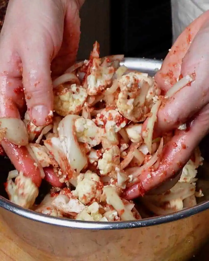 A woman tossing cauliflower and onions with tomato paste and spices.