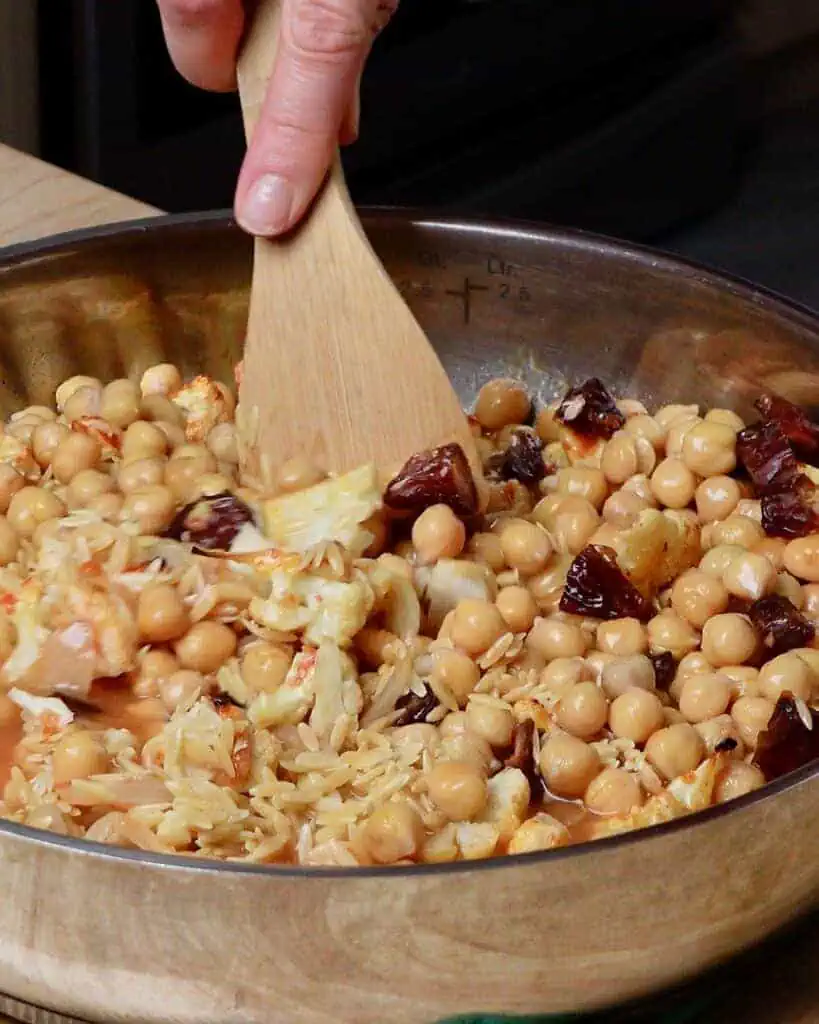 Stirring a pan of baked orzo with dried fruit and chickpeas.