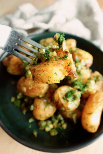 Crispy dill roasted potatoes on a plate, with one close-up on a fork.