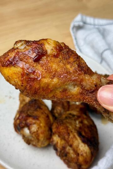 A woman holding an air fryer chicken drumstick over a plate.
