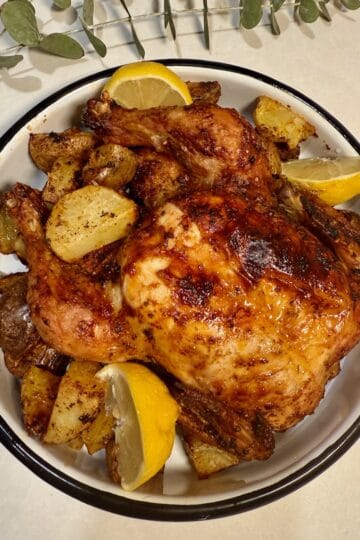 Air fryer whole chicken with potatoes and lemons on a white serving dish.