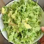 A woman holding a serving bowl with the finished arugula salad.