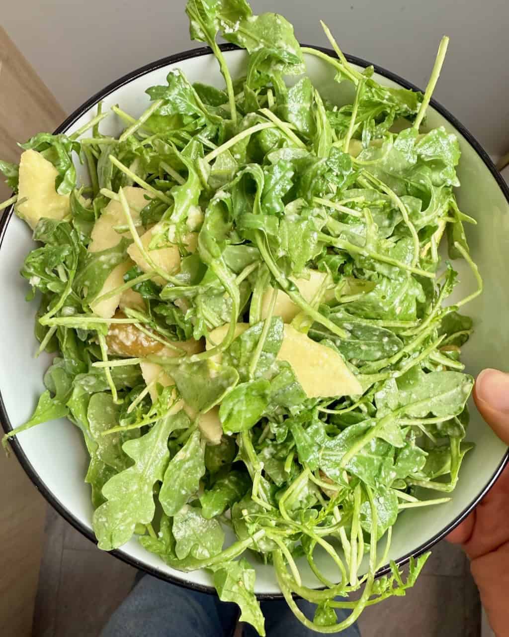 A woman holding a serving bowl with the finished arugula salad.