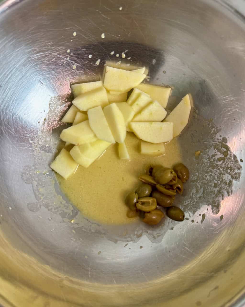 Sliced apples and olives in a stainless steel bowl with lemon dijon dressing.