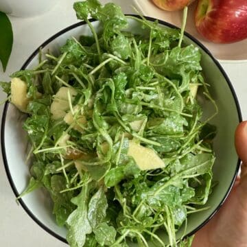 A woman holding a serving bowl with the finished arugula salad.