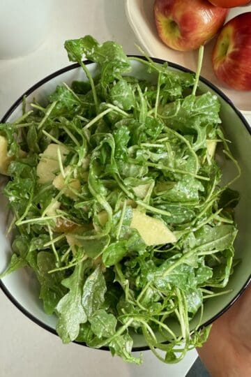 A woman holding a serving bowl with the finished arugula salad.