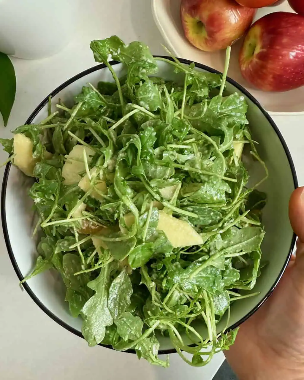 A woman holding a serving bowl with the finished arugula salad.