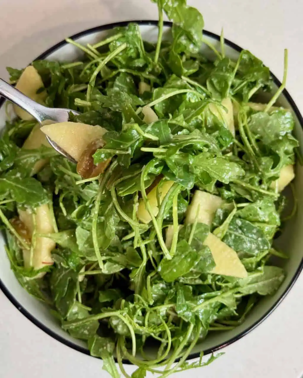 Arugula, apple, and olive salad in a bowl with a fork.