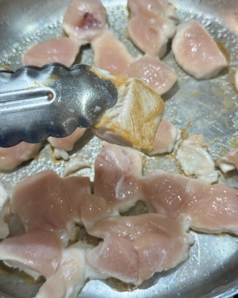 Showing the golden brown sear on a piece of chicken while the other pieces cook in the background.