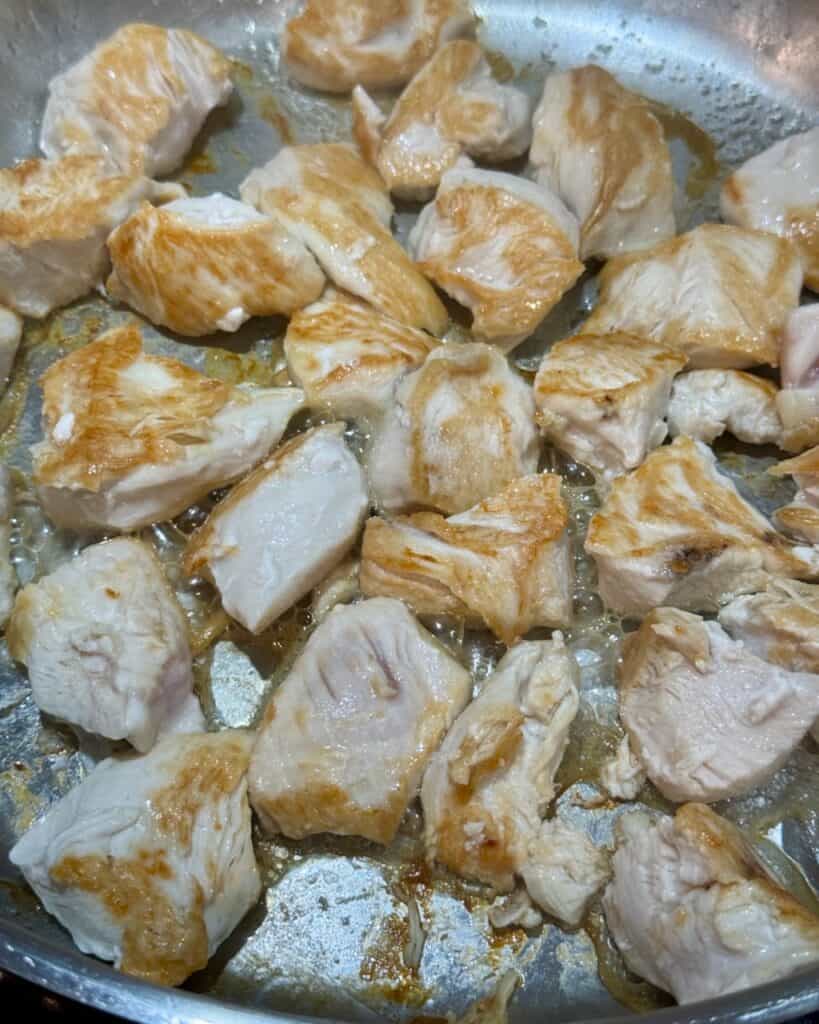 Seared cubes of chicken breast in a pan.