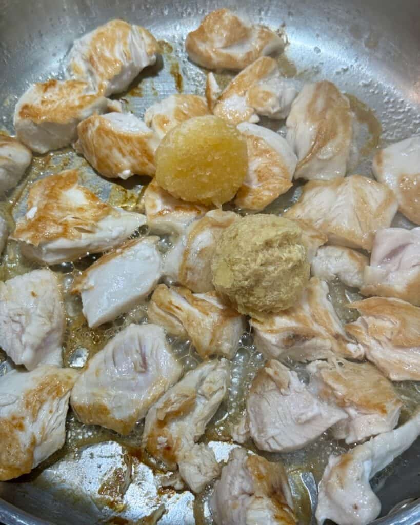 Adding the garlic and ginger to the seared chicken in the pan.