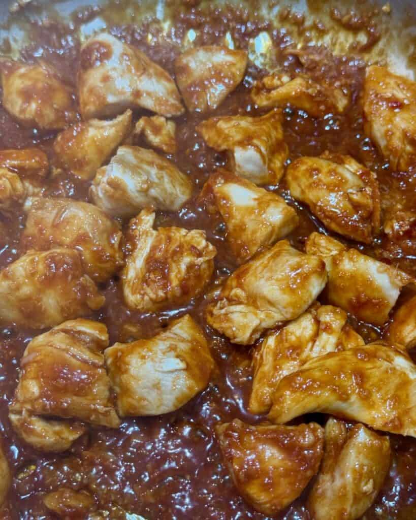 Tossing the chicken with the gochujang sauce in a pan.