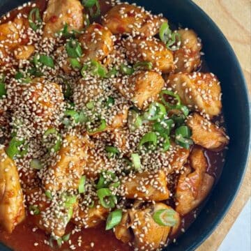 A plate of gochujang chicken with sesame seeds and green onions.