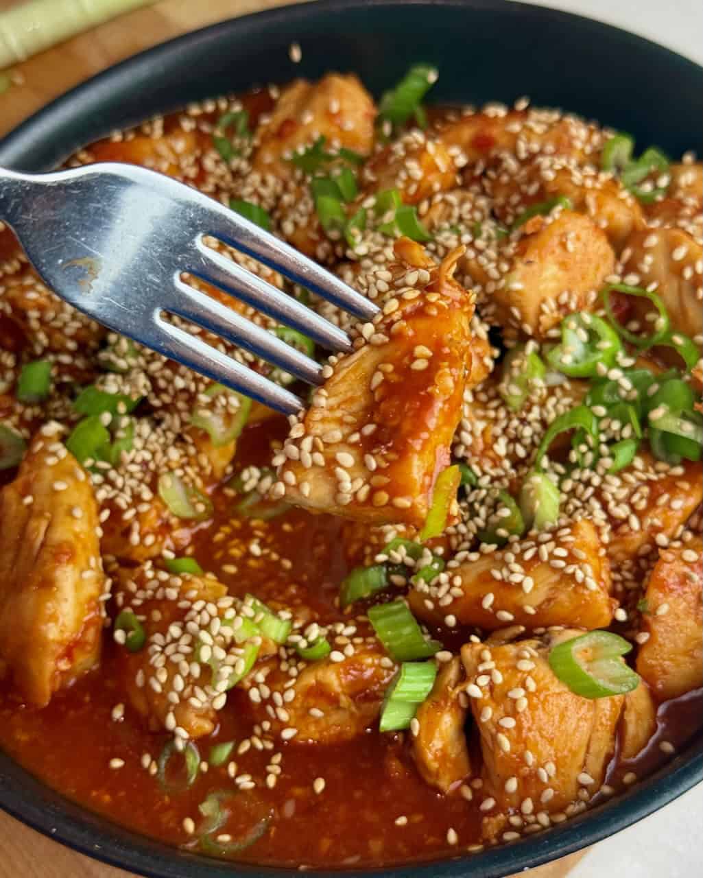A piece of gochujang chicken on a fork over the bowl