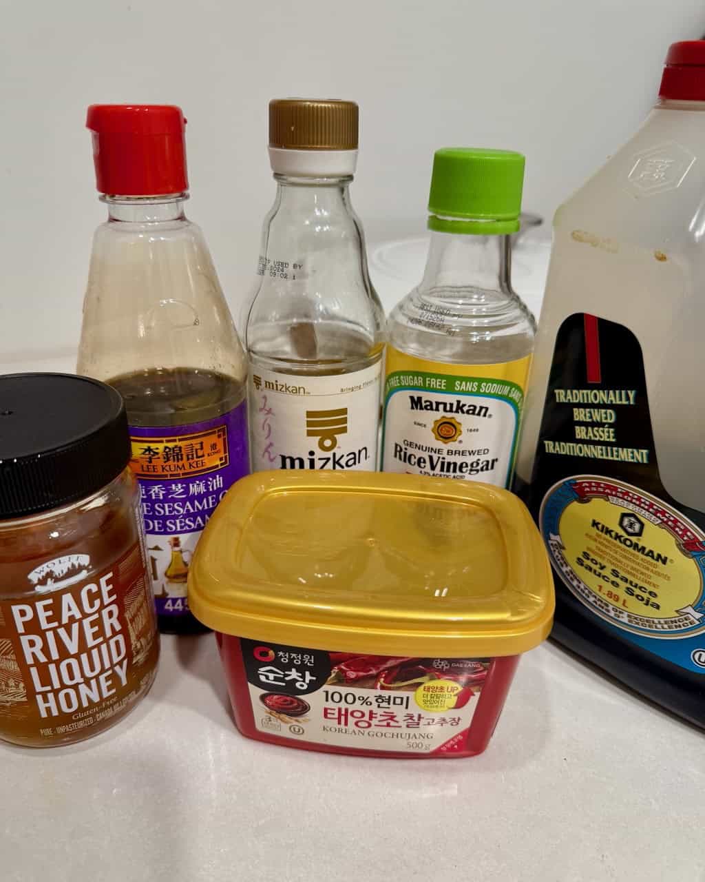 Honey, sesame oil, mirin, rice vinegar, soy sauce, and gochujang, lined up.