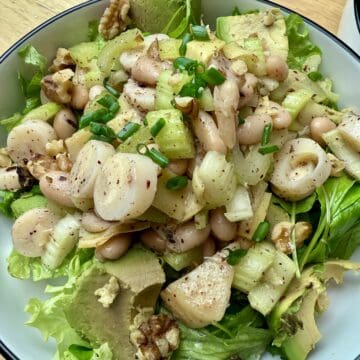 A large bowl of hearts of palm and white bean salad on a bed of arugula.