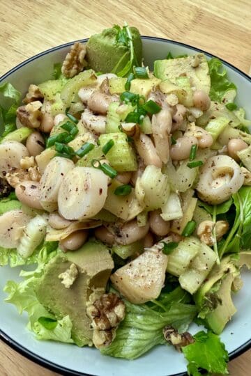 A large bowl of hearts of palm and white bean salad on a bed of arugula.