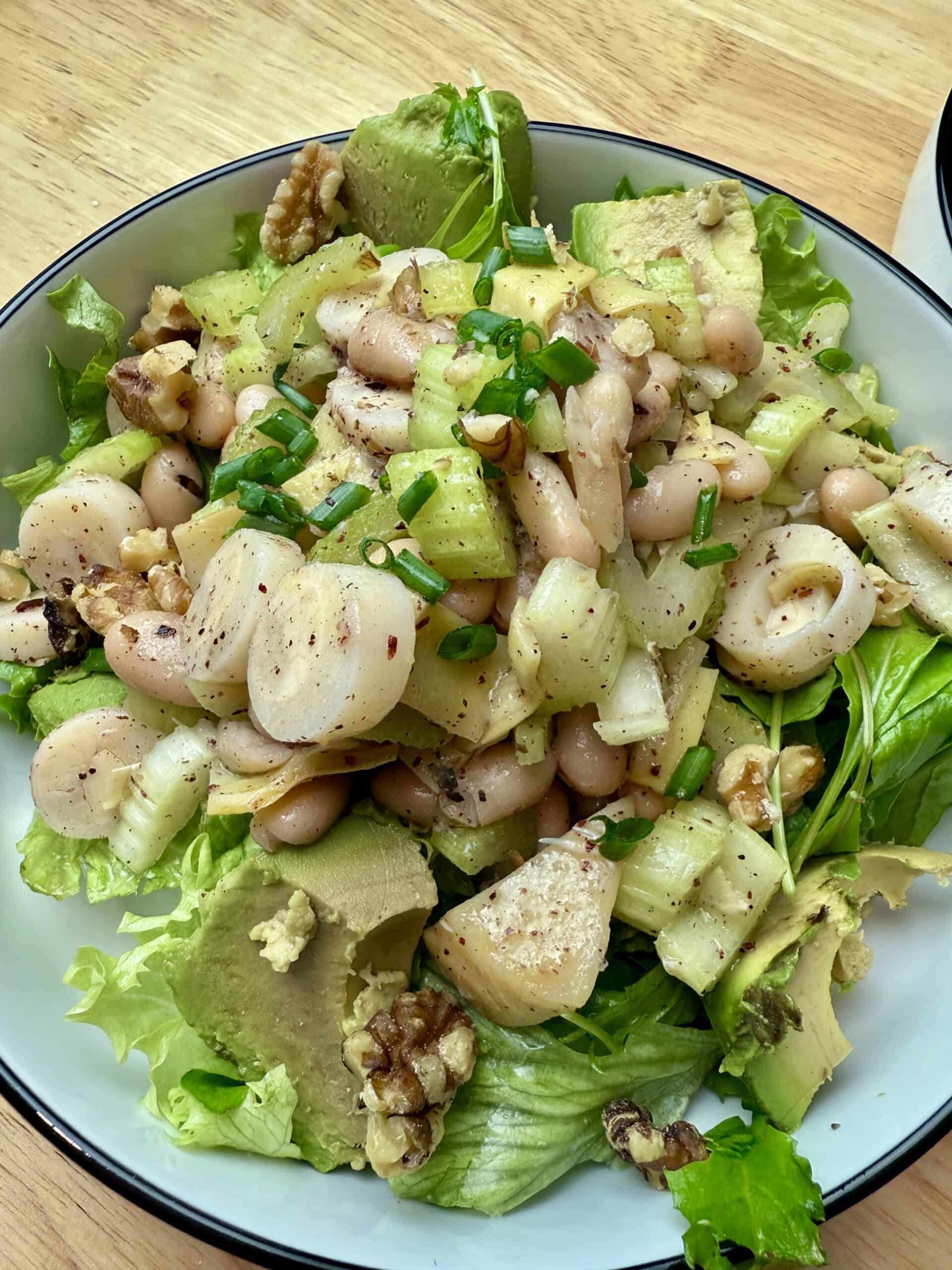 A large bowl of hearts of palm and white bean salad on a bed of arugula.