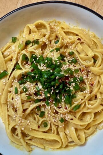 Nutritional yeast noodles garnished with green onions and sesame seeds in a white bowl.