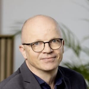 Klar mand med briller i forretningsdragt, professionelt udseende, baggrund med planter.