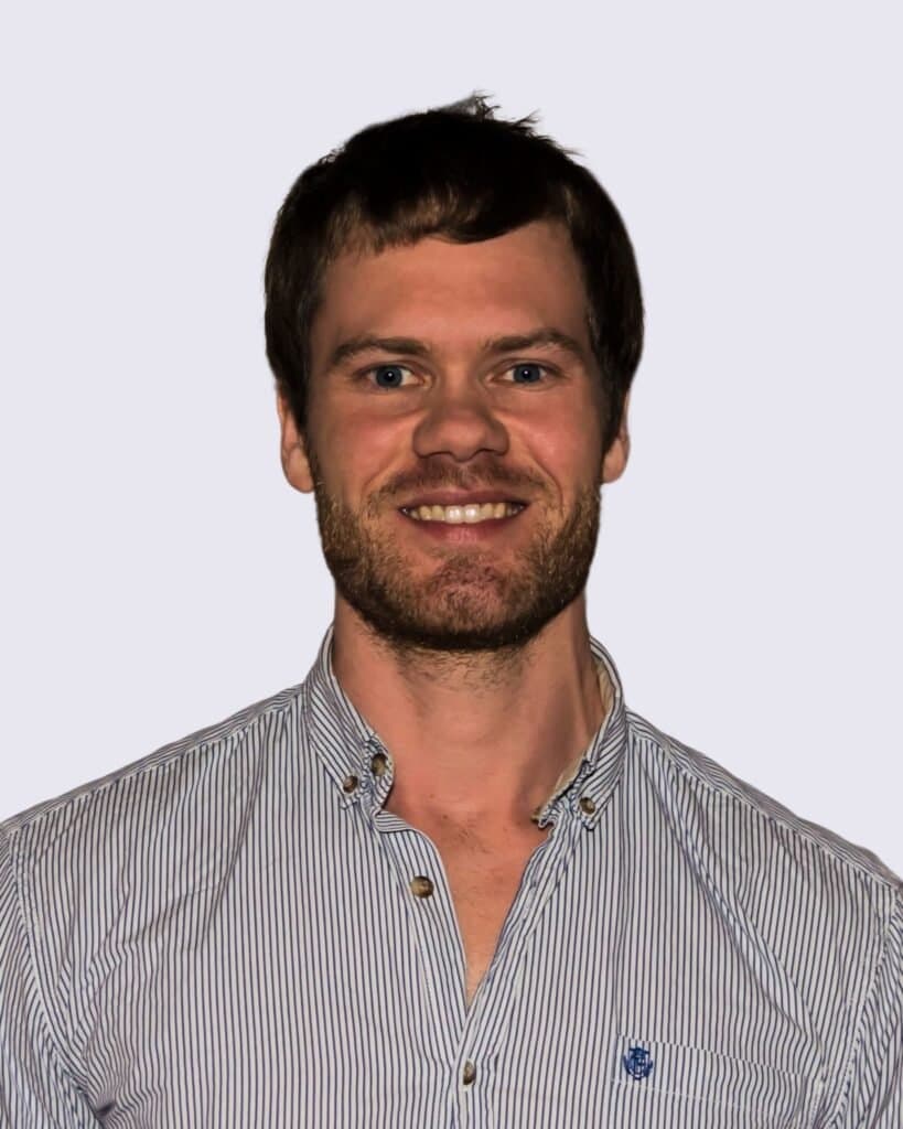 Menneskelig portræt af en ung mand med kort mørkt hår og skæg, i casual skjorte, smilende og professionel.