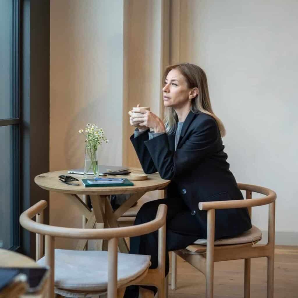 1. Kvinde sidder med kop kaffe i et moderne café, iført business outfit, afslappet atmosfære.